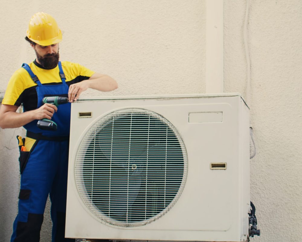 Expert wireman starting work on malfunctioning air conditioner, using hand drill to take apart condenser coil panel. Competent mechanic dismantling hvac system to check for faulty wires