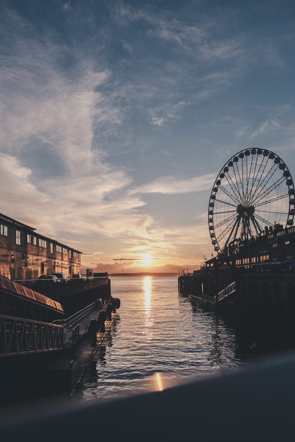 A vertical shot of the sea with a ferries wheel in the distance under a blue sky